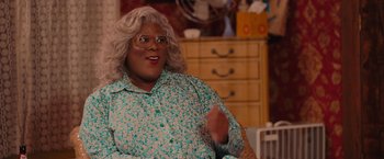 Movie still from “Tyler Perry's A Madea Homecoming” (2022), directed by Tyler Perry – A man with blonde hair and glasses sitting in a chair; Medium shot, Over the shoulder angle