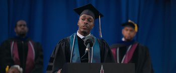 Movie still from “Tyler Perry's A Madea Homecoming” (2022), directed by Tyler Perry – A man wearing a graduation cap and gown while standing at a podium; Medium shot, Low angle