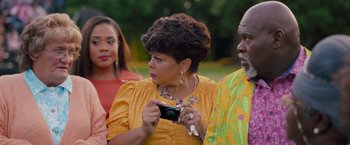 Movie still from “Tyler Perry's A Madea Homecoming” (2022), directed by Tyler Perry – A woman holding a camera while standing next to two other people; Close Up shot, Over the shoulder angle
