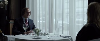 Movie still from “Tár” (2022), directed by Todd Field – A man sitting at a table with a glass of wine; Medium shot, Over the shoulder angle