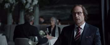 Movie still from “Tár” (2022), directed by Todd Field – A man sitting at a table with a glass of wine in front of him; Close Up shot, Over the shoulder angle