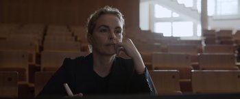 Movie still from “Tár” (2022), directed by Todd Field – A woman sitting at a table in front of an audience; Close Up shot, Low angle