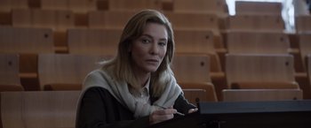 Movie still from “Tár” (2022), directed by Todd Field – A woman sitting at a table in front of rows of chairs; Medium shot, Low angle