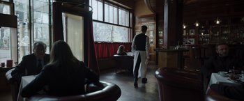 Movie still from “Tár” (2022), directed by Todd Field – A man walking in front of a window while a woman sits on a chair; Wide shot, Over the shoulder angle