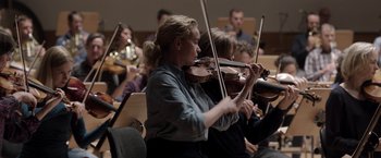 Movie still from “Tár” (2022), directed by Todd Field – A group of people playing musical instruments in an orchestra; Medium shot, Low angle