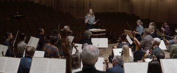Movie still from “Tár” (2022), directed by Todd Field – A woman is conducting a orchestra in front of an audience; Wide shot, Low angle