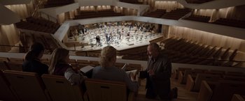 Movie still from “Tár” (2022), directed by Todd Field – Two people are sitting in chairs in front of an orchestra; Wide shot, High angle