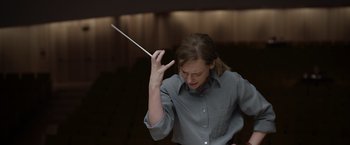 Movie still from “Tár” (2022), directed by Todd Field – A woman is holding a conductor's baton up; Medium shot, Low angle