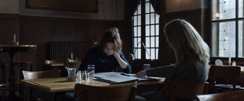 Movie still from “Tár” (2022), directed by Todd Field – A woman sitting at a table looking at a menu; Medium shot, Over the shoulder angle