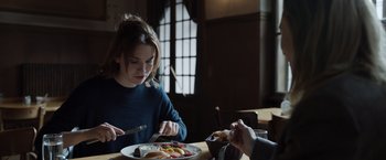 Movie still from “Tár” (2022), directed by Todd Field – A woman sitting at a table with a plate of food in front of her; Medium shot, Over the shoulder angle