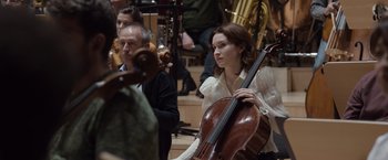 Movie still from “Tár” (2022), directed by Todd Field – A woman holding a cello in front of other people; Medium shot, Low angle