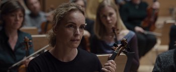 Movie still from “Tár” (2022), directed by Todd Field – A woman is holding a violin in front of other people; Close Up shot, Over the shoulder angle