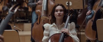 Movie still from “Tár” (2022), directed by Todd Field – A woman is holding a cello in front of a man; Medium shot, Over the shoulder angle
