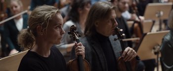 Movie still from “Tár” (2022), directed by Todd Field – A woman holding a violin in front of a crowd of people; Close Up shot, Low angle