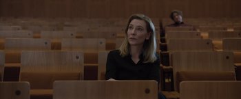 Movie still from “Tár” (2022), directed by Todd Field – A woman in a black shirt is sitting in a lecture hall; Medium shot, Over the shoulder angle