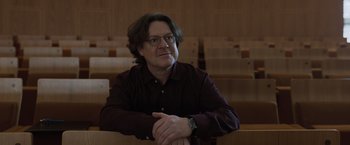 Movie still from “Tár” (2022), directed by Todd Field – A man sitting in front of a wooden wall in a room; Close Up shot, Low angle