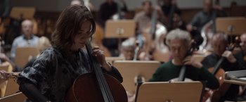 Movie still from “Tár” (2022), directed by Todd Field – A woman holding a cello in a room full of people; Medium shot, Low angle