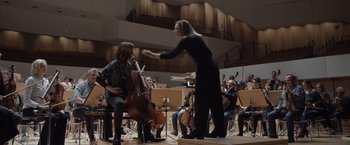 Movie still from “Tár” (2022), directed by Todd Field – A woman in a black dress is playing the cello in front of a group of people; Wide shot, Low angle