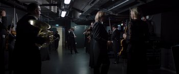 Movie still from “Tár” (2022), directed by Todd Field – A group of people standing in a room with musical instruments; Wide shot, Low angle