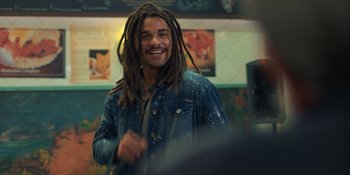 A man with dreads is smiling for the camera