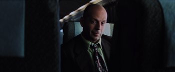 Movie still from “Unbreakable” (2000), directed by M. Night Shyamalan – A man in a suit and tie sitting on a bus; Close Up shot, Over the shoulder angle