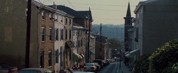 Movie still from “Unbreakable” (2000), directed by M. Night Shyamalan – A city street lined with parked cars on a sunny day; Extreme Wide shot, High angle