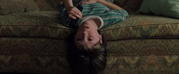 Movie still from “Unbreakable” (2000), directed by M. Night Shyamalan – A young boy laying on a couch holding a remote control; Close Up shot, High angle