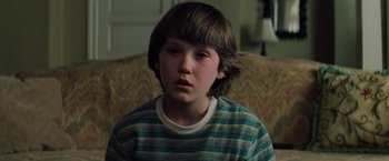 Movie still from “Unbreakable” (2000), directed by M. Night Shyamalan – A young boy sitting on a couch in front of a window; Close Up shot, High angle