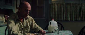 Movie still from “Unbreakable” (2000), directed by M. Night Shyamalan – A man sitting at a table with a bottle of milk; Medium shot, Low angle