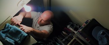 Movie still from “Unbreakable” (2000), directed by M. Night Shyamalan – A bald man sitting on a bed looking at a computer; Medium shot, Overhead angle