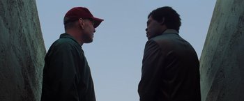 Movie still from “Unbreakable” (2000), directed by M. Night Shyamalan – Two men are facing each other and one is wearing a red hat; Medium shot, Low angle