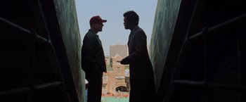 Movie still from “Unbreakable” (2000), directed by M. Night Shyamalan – Two men talking to each other in front of a building; Wide shot, Low angle