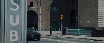 Movie still from “Unbreakable” (2000), directed by M. Night Shyamalan – A man is crossing the street in front of a brick building; Extreme Wide shot, High angle