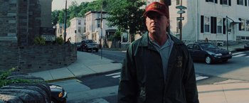 Movie still from “Unbreakable” (2000), directed by M. Night Shyamalan – A man wearing a hat standing on the side of the street; Medium shot, Low angle