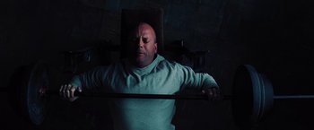 Movie still from “Unbreakable” (2000), directed by M. Night Shyamalan – A bald man holding onto a bar in a dark room; Medium shot, Overhead angle
