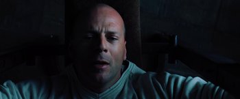 Movie still from “Unbreakable” (2000), directed by M. Night Shyamalan – A man with a bald head is sitting in a dark room; Close Up shot, Overhead angle