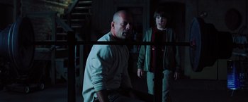 Movie still from “Unbreakable” (2000), directed by M. Night Shyamalan – A man and a boy are standing in a dark room; Medium shot, Over the shoulder angle
