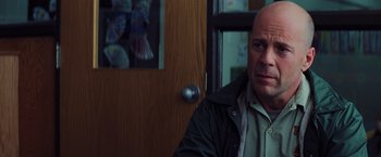 Movie still from “Unbreakable” (2000), directed by M. Night Shyamalan – A bald man in a black jacket in front of a wooden door; Close Up shot, Over the shoulder angle