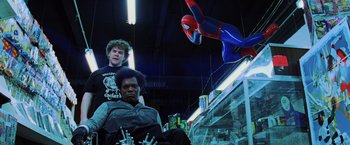 Movie still from “Unbreakable” (2000), directed by M. Night Shyamalan – A man sitting next to another man in front of a spider - man statue; Medium shot, Low angle
