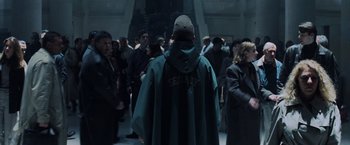 Movie still from “Unbreakable” (2000), directed by M. Night Shyamalan – A man in a green rain coat is standing in front of a group of people; Wide shot, High angle