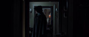 Movie still from “Unbreakable” (2000), directed by M. Night Shyamalan – A man in a hooded cloak walking in a dark room; Medium shot, Over the shoulder angle