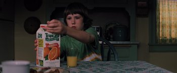 Movie still from “Unbreakable” (2000), directed by M. Night Shyamalan – A young boy sitting at a table with a glass of orange juice; Medium shot, Over the shoulder angle