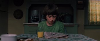 Movie still from “Unbreakable” (2000), directed by M. Night Shyamalan – A boy sitting at a table with a glass of orange juice; Close Up shot, Over the shoulder angle