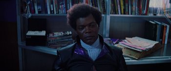 Movie still from “Unbreakable” (2000), directed by M. Night Shyamalan – A man in a black jacket is sitting in front of a book shelf; Close Up shot, Low angle