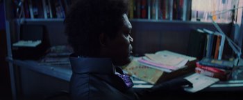 Movie still from “Unbreakable” (2000), directed by M. Night Shyamalan – A man sitting at a desk in front of books; Close Up shot, Over the shoulder angle