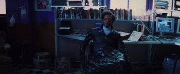 Movie still from “Unbreakable” (2000), directed by M. Night Shyamalan – A man sitting in a chair in a room with books; Medium shot, High angle