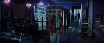 Movie still from “Unbreakable” (2000), directed by M. Night Shyamalan – A man standing in front of a wall of comic books; Wide shot, Low angle