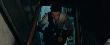 Movie still from “Uncharted” (2022), directed by Ruben Fleischer – A man in a suit and tie holding a bag of food; Medium shot, Overhead angle