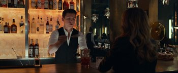 Movie still from “Uncharted” (2022), directed by Ruben Fleischer – A man in a black vest is at a bar with a woman; Medium shot, Over the shoulder angle