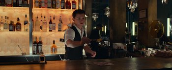 Movie still from “Uncharted” (2022), directed by Ruben Fleischer – A man standing at a bar preparing a drink; Medium shot, Low angle